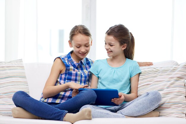 people, children, technology, friends and friendship concept - happy little girls with tablet pc computer sitting on sofa at home