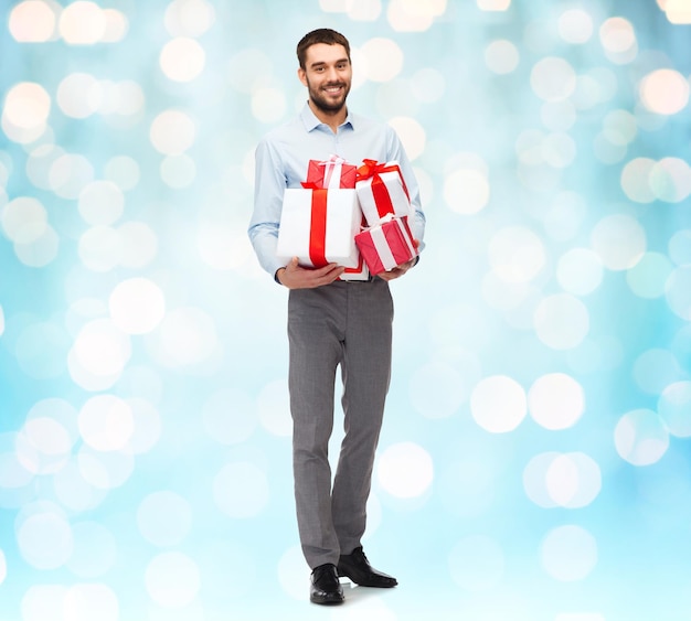 people, christmas, birthday and holidays concept - happy young man holding gift boxes over blue lights background