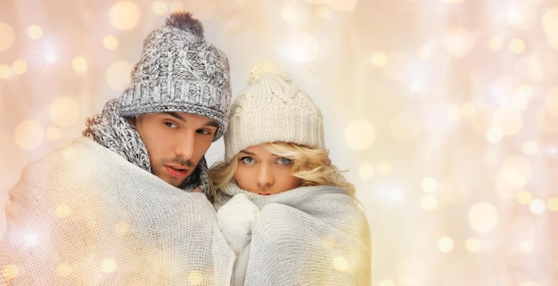 people, christmas, holidays and new year concept - freezing couple in winter clothes wrapped in plaid over holidays lights background