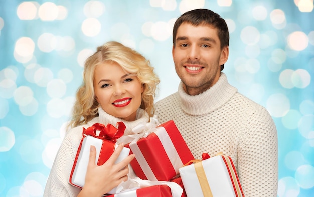 people, christmas, holidays and new year concept - happy family couple in sweaters holding gifts or presents over blue lights background