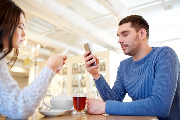 people, communication and dating concept - couple with smartphones drinking tea at cafe or restaurant