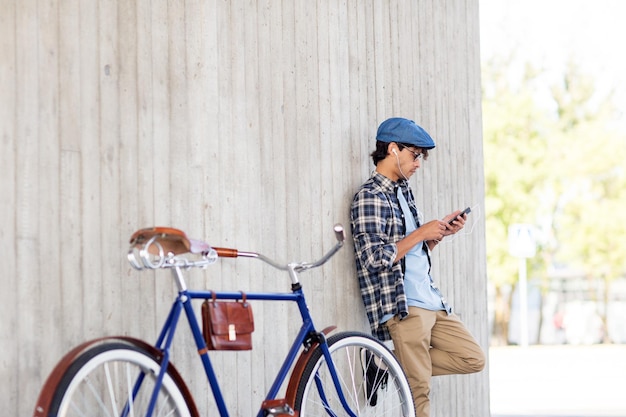 people, communication, technology and lifestyle - hipster man with smartphone, earphones and fixed gear bike listening to music on city street