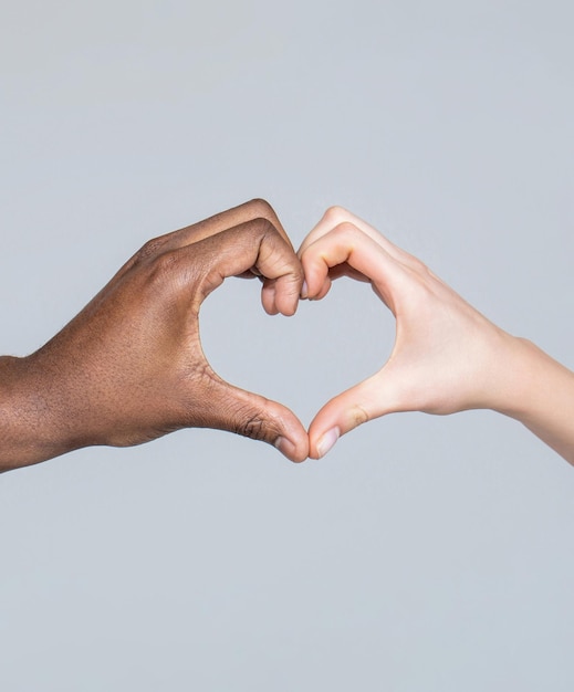 People different skin colors put their hands together making heart shape in white background Closeup of female and male hands of different skin color making heart shape