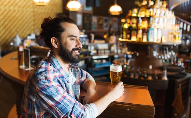 people, drinks, alcohol and leisure concept - happy young man drinking beer at bar or pub