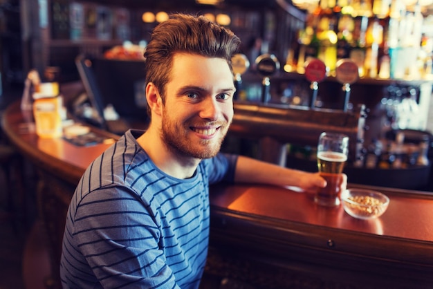 people, drinks, alcohol and leisure concept - happy young man drinking beer at bar or pub