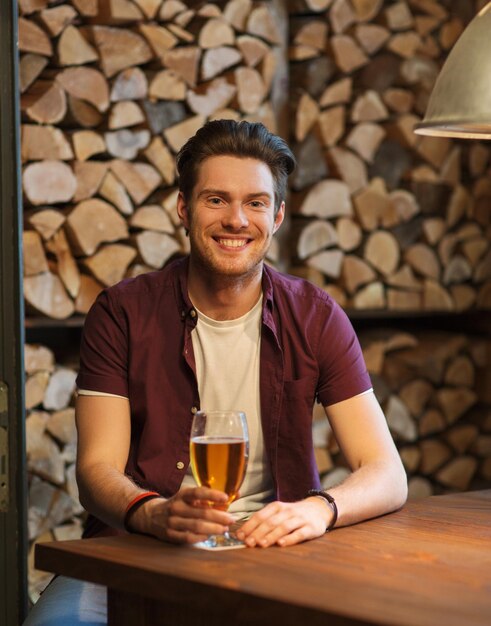 people, drinks, alcohol and leisure concept - happy young man drinking beer at bar or pub