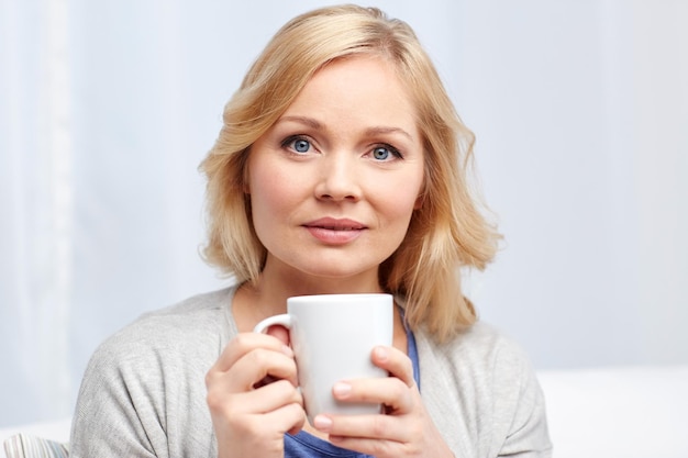 people, drinks and leisure concept - woman with cup of tea or coffee at home