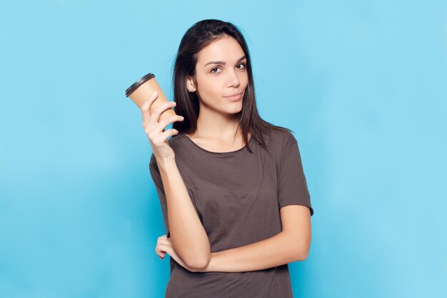 people drinks and lifestyle concept Young beautiful woman with coffe over blue background Happy and smiling attractive woman woman with dark hair is holding a cardboard glass with coffee