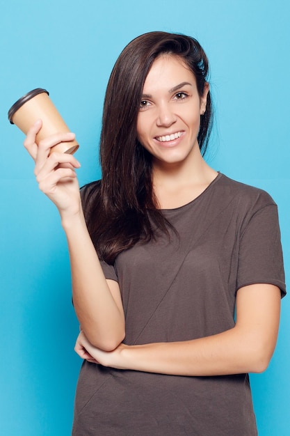 people drinks and lifestyle concept Young beautiful woman with coffe over blue background Happy and smiling attractive woman woman with dark hair is holding a cardboard glass with coffee