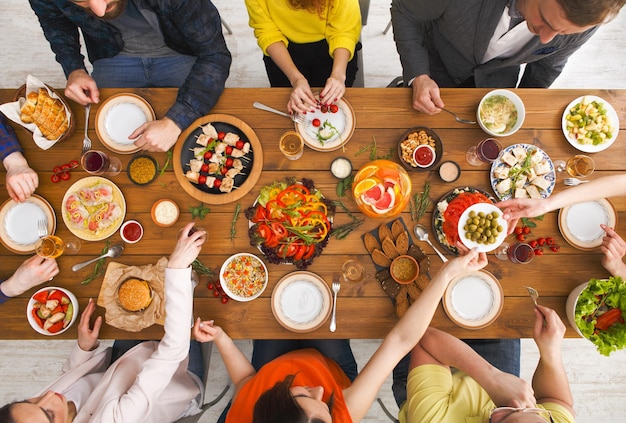 People eat healthy meals at festive table served for party. Friends celebrate with organic food on wooden table top view. Happy company having lunch, taking salad dish