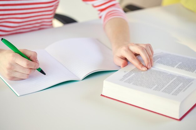 people and education concept - close up of female hands with book or textbook writing to notebook at school