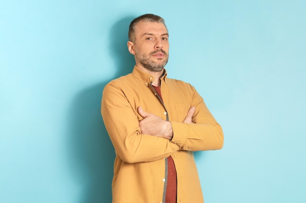 People emotions concept Portrait of serious mature man posing with folded arms standing on blue studio background