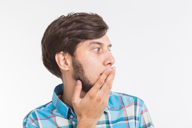 People, emotions and gesture concept - young surprised man covering his mouth with his hand on white background.