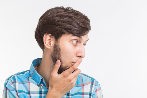 People, emotions and gesture concept - young surprised man covering his mouth with his hand on white background.