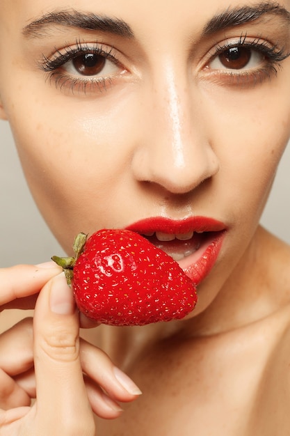 People, emotions, natural, food, beauty and lifestyle concept - Sexy Woman Eating Strawberry. Sensual Lips. Manicure and Lipstick. Desire. Beauty Girl Sexy Lips with Strawberry. white teeth