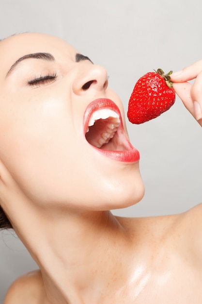 People, emotions, natural, food, beauty and lifestyle concept - Sexy Woman Eating Strawberry. Sensual Lips. Manicure and Lipstick. Desire. Beauty Girl Sexy Lips with Strawberry. white teeth