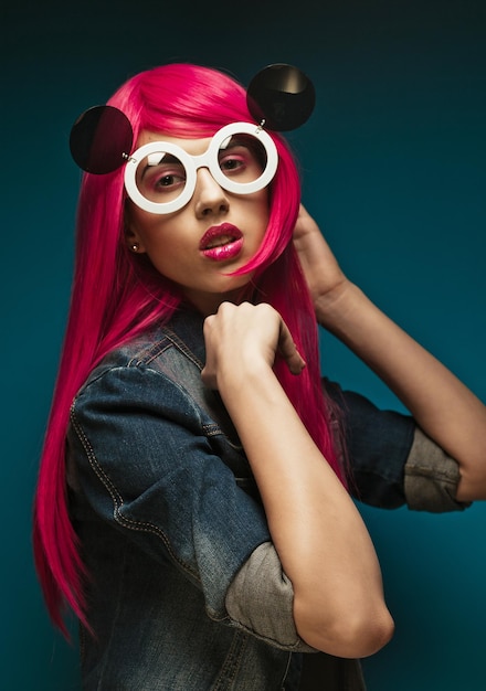 People and fashion concept fashion model with pink hair and big sunglasses over blue background