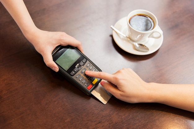 people, finance, technology and consumerism concept - close up of waitress holding credit card reader and customer hand entering pin code at cafe