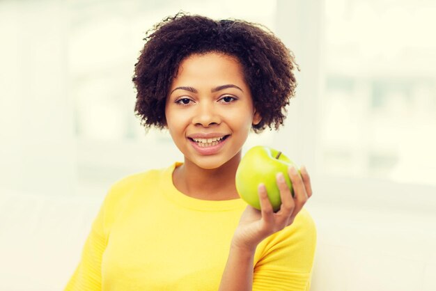 people, food, healthy eating and dental care concept - happy african american young woman with green apple at home