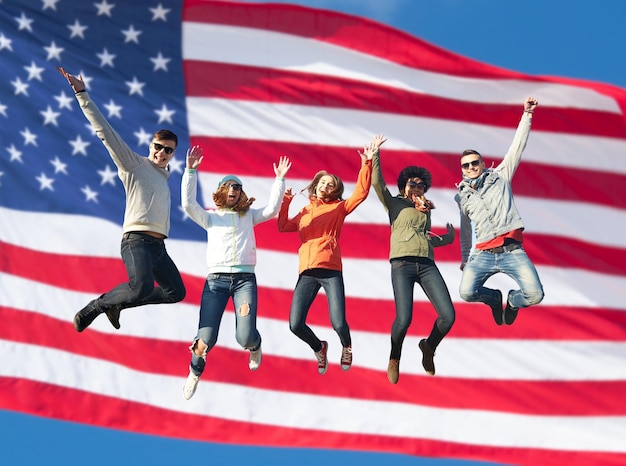 people, freedom, happiness and teenage concept - group of happy international friends in sunglasses jumping high over american flag background