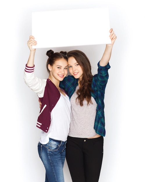 people, friends, teens and friendship concept - happy smiling pretty teenage girls holding and showing white blank board