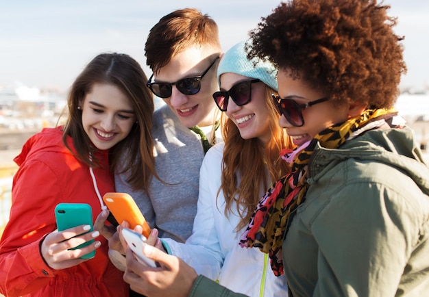 people, friendship, cloud computing and technology concept - group of smiling teenage friends with smartphone outdoors