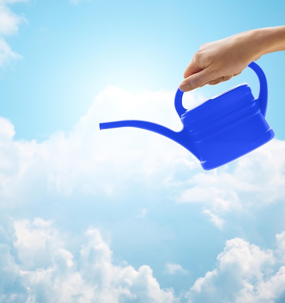 people, gardening and profession concept - close up of woman or gardener hand holding watering can over blue sky with clouds