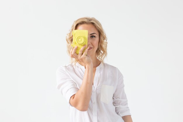 Photo people, hobby and fashion concept - beautiful girl with blue hair hold yellow retro camera on white wall