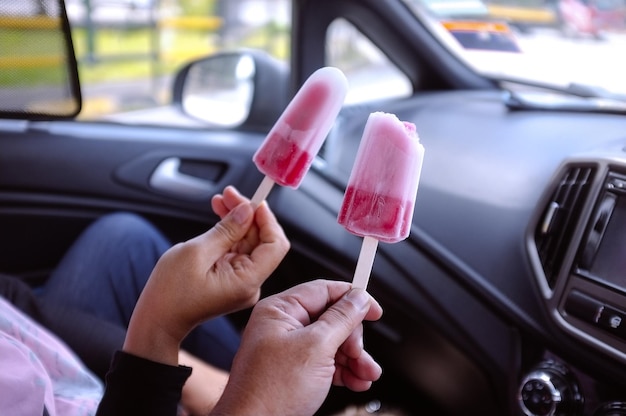 People holding pink ice cream sticks in the car