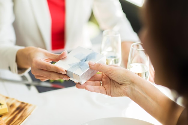 people, holidays, celebration and lifestyle concept - close up of women giving birthday present at restaurant