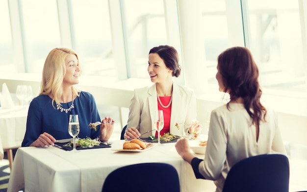 people, holidays, celebration and lifestyle concept - happy women eating and drinking champagne at restaurant