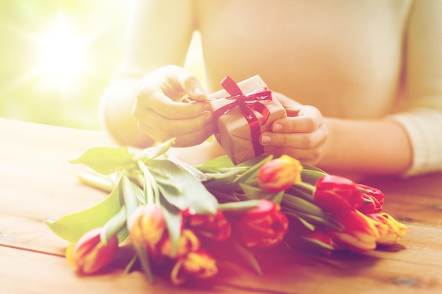 people, holidays and greeting concept - close up of woman holding gift box and tulip flowers