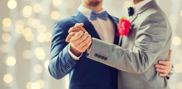 people, homosexuality, same-sex marriage and love concept - close up of happy male gay couple holding hands and dancing on wedding over holidays lights background