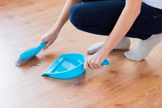 people, housework, cleaning and housekeeping concept - close up of woman with brush and dustpan sweeping floor at home