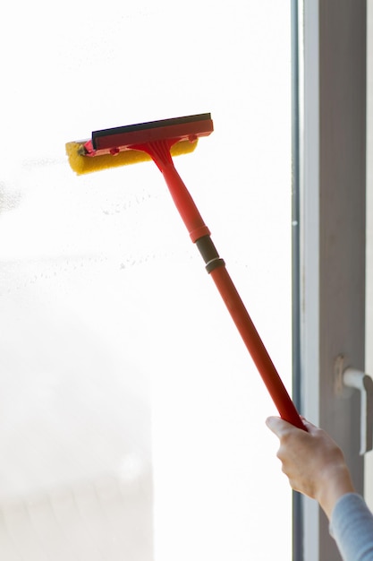 people, housework and housekeeping concept -close up of hand cleaning window with sponge mop