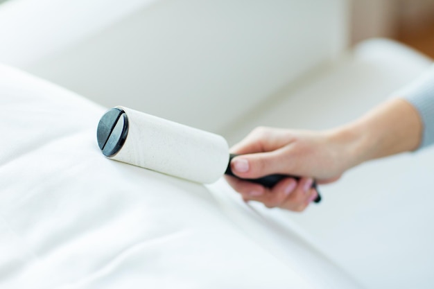 people, housework and housekeeping concept - close up of woman hand with sticky roller cleaning furniture textile