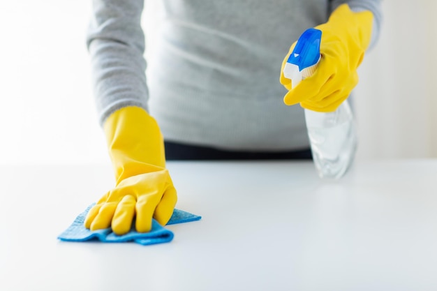 people, housework and housekeeping concept - close up of woman hands cleaning table with cloth and detergent spray at home