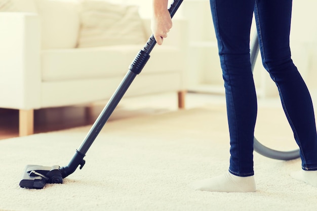 people, housework and housekeeping concept - close up of woman with legs vacuum cleaner cleaning carpet at home