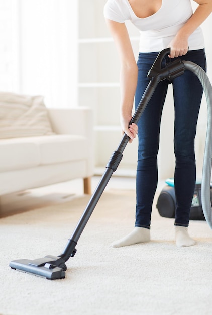 people, housework and housekeeping concept - close up of woman with vacuum cleaner cleaning carpet at home