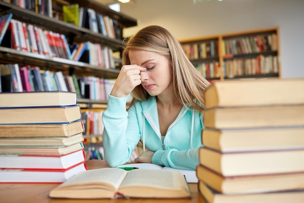 people, knowledge, education, literature and school concept - bored student girl or young woman with books dreaming in library