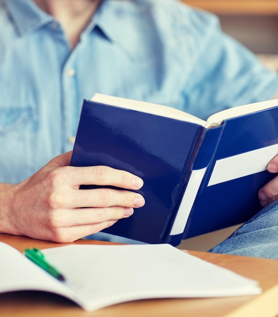 people, knowledge, education and school concept - close up of student reading book at school library