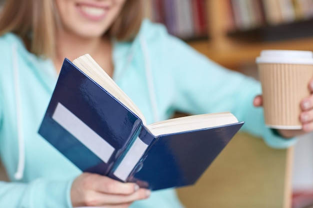 people, knowledge, education and school concept - close up of student reading book at school library