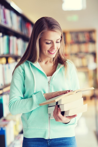 people, knowledge, education and school concept - happy student girl or young woman with book in library