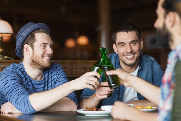 people, leisure, celebration, friendship and bachelor party concept - happy male friends drinking beer and clinking bottles at bar or pub