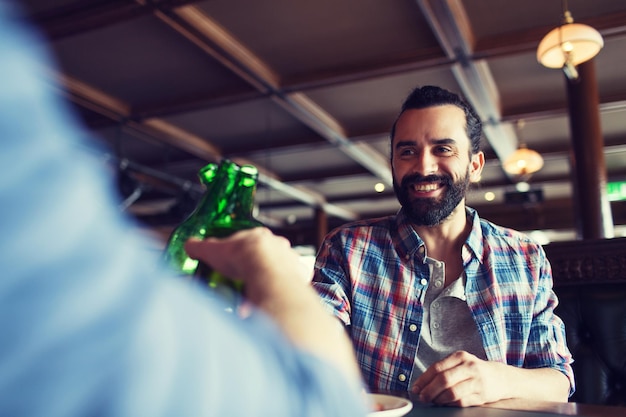 people, leisure, celebration, friendship and bachelor party concept - happy male friends drinking beer and clinking bottles at bar or pub