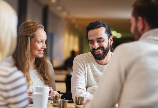 people, leisure, communication, eating and drinking concept - happy friends meeting and drinking tea or coffee at cafe