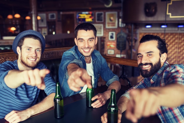 people, leisure, friendship and bachelor party concept - happy male friends drinking bottled beer and  and pointing on you at bar or pub