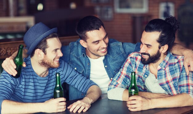 people, leisure, friendship and bachelor party concept - happy male friends drinking bottled beer and talking at bar or pub