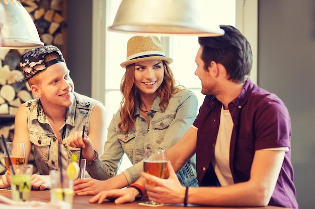 people, leisure, friendship and communication concept - group of happy smiling friends drinking beer and cocktails at bar or pub