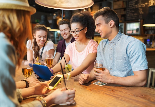 people, leisure, friendship and communication concept - group of happy smiling friends with tablet pc computer and drinks at bar or pub